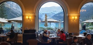 A restaurant with large arched windows offering views of mountains and a lake.
