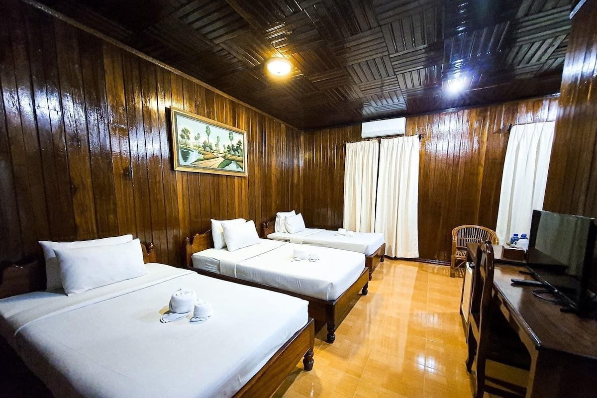 A hotel room with two beds, wooden walls, a painting, a TV, and a chair.