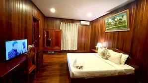 A hotel room with wooden paneling, a bed with white linens, a television on a wooden table, and a wardrobe. - Sam Moon's Hotel Angkor (Siem Reap)