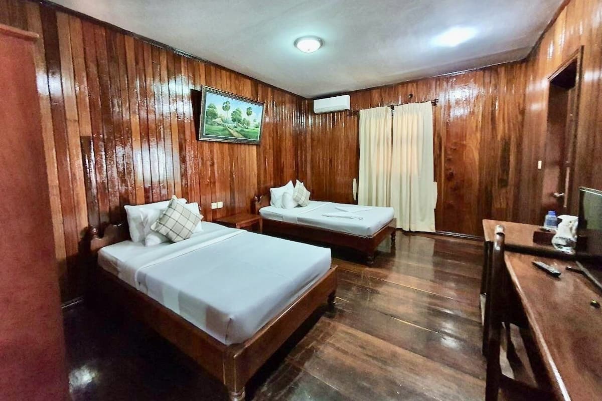 A room with two wooden beds, a desk with a chair, and a television.