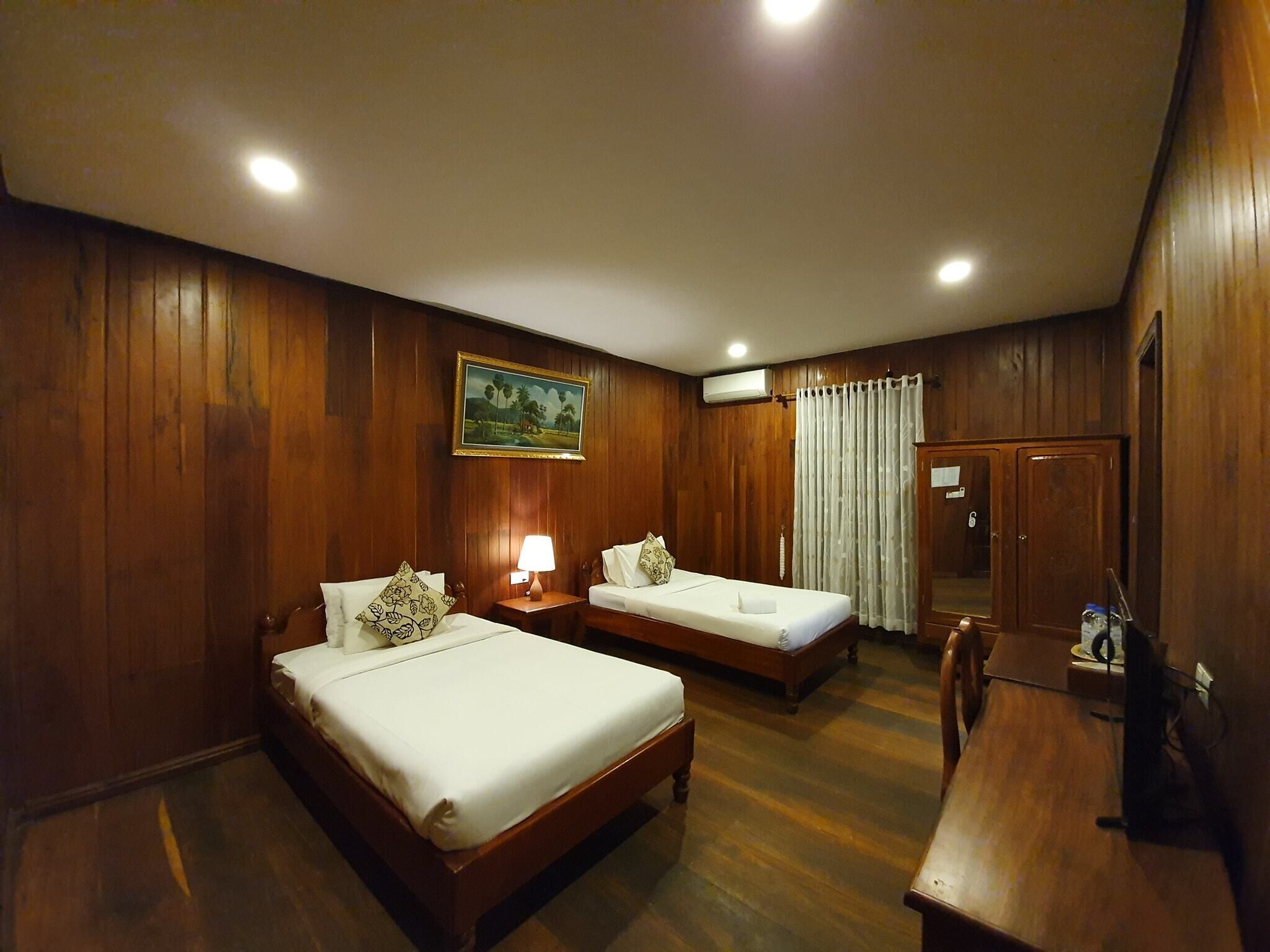 A hotel room with two wooden beds, a desk, and a mirror.