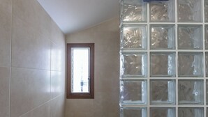 Un baño con paredes de azulejos, un ventanal y un separador de bloques de vidrio.