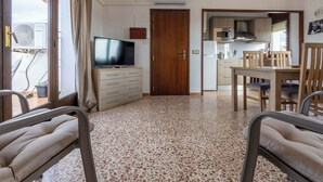 Un espacio habitable compacto con kitchenette, comedor y televisor sobre un tocador.