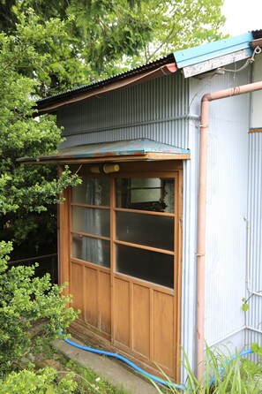 Una ventana de madera con techo de metal, rodeada de follaje y un muro de metal corrugado.