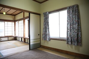 Una habitación japonesa tradicional con suelo de tatami, puertas correderas y una ventana con cortinas estampadas.