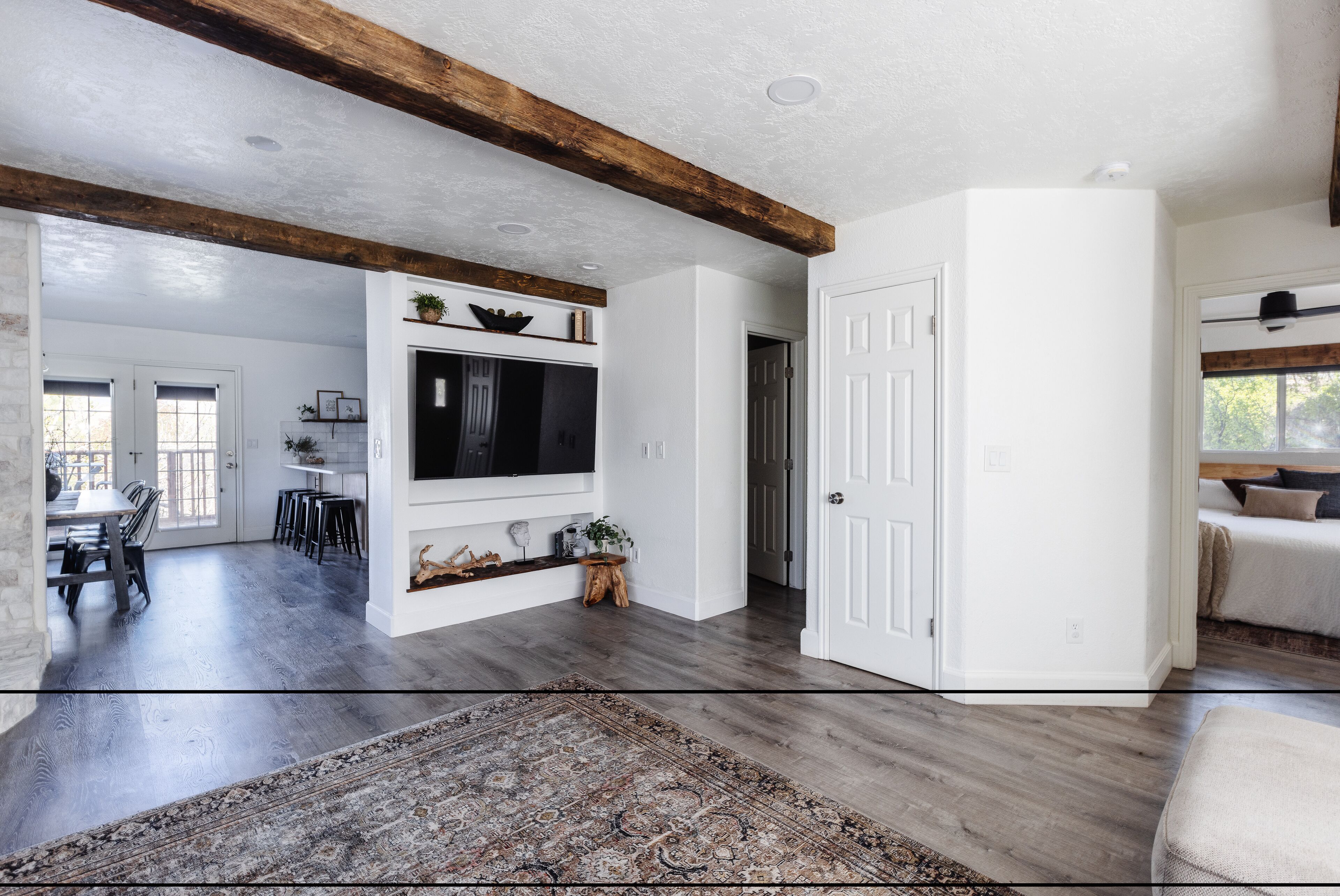 A spacious living area with a wooden ceiling, a large flat-screen TV mounted on the wall, and a dining area with a table and chairs.