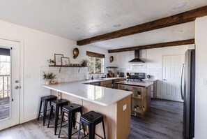 Una cucina moderna con un'isola grande, sgabelli da bar, travi in legno, mobili bianchi e un frigorifero in acciaio inossidabile.