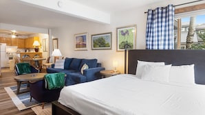 Une chambre d’hôtel avec un lit, un canapé, une petite table, une lampe et une vue sur la cuisine et le balcon.