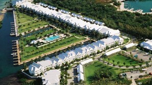 Eine Vogelperspektive zeigt ein Resort mit mehreren Gebäuden mit weißen Dächern, einem zentralen Pool und einer Anlegestelle, die ins Wasser führt.