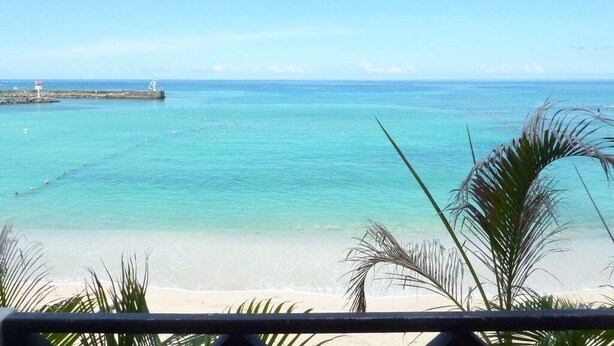 A beach view with clear turquoise water, a sandy shore, and a distant pier.