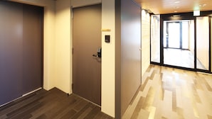 A hallway with a door marked '102', a wall-mounted intercom, and a wooden ceiling.