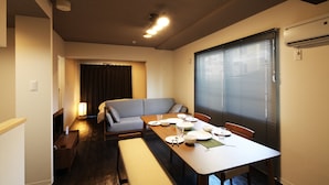 A dining area with a table set for four, a bench, a sofa, and a window with blinds.