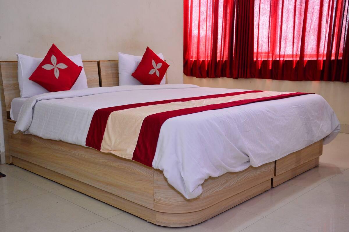 Una cama con estructura de madera, ropa de cama blanca y detalles en rojo.
