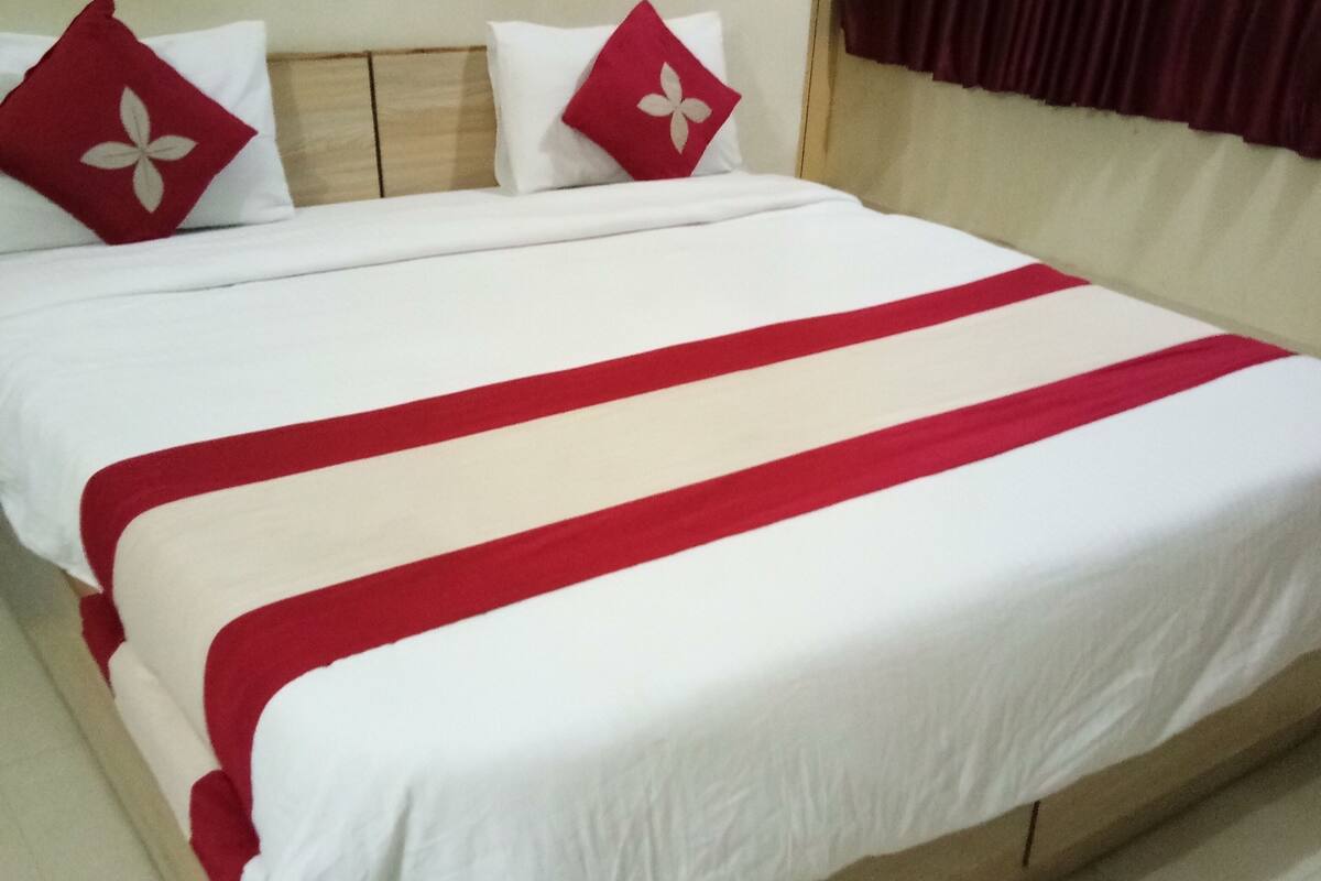 Una cama con ropa de cama blanca y roja, dos almohadas con diseños florales y un cabecero de madera.