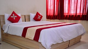 Ein ordentlich bezogenes Bett mit Holzrahmen, weißer Bettwäsche und roten Akzenten.