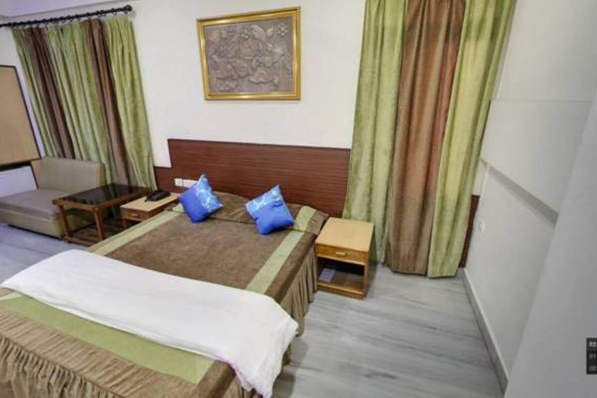 Habitación de hotel con cama, una mesita pequeña, una silla y un escritorio. Hay un cuadro en la pared y cortinas en las ventanas.