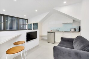 A modern kitchen with a built-in oven and a dishwasher, a grey sofa, and two wooden stools. - One bedroom  in Australia, Surry Hills (Surry Hills)