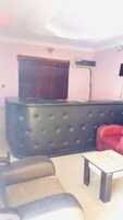 A living room with a dark tufted sofa, a red chair, a wooden coffee table, and a pink wall with a window and an air conditioning unit.
