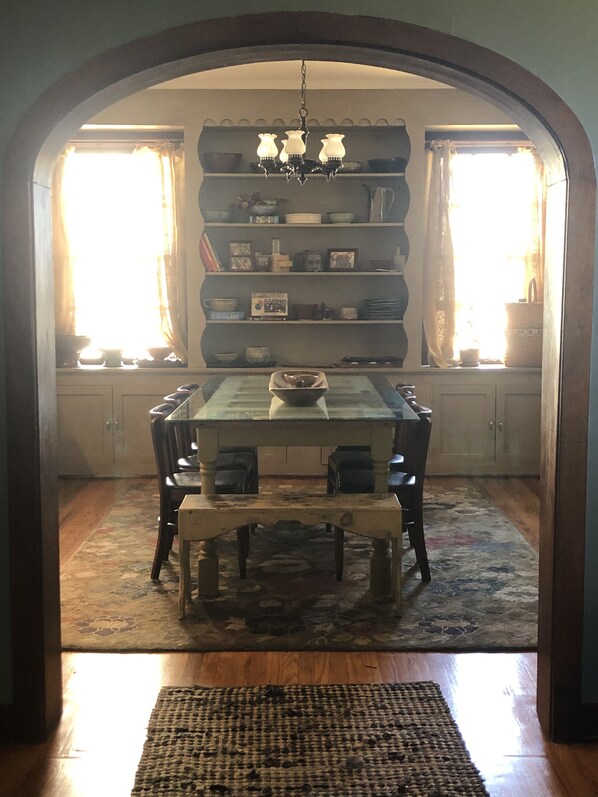 A dining area with a table and chairs, a chandelier, and shelves with various items.