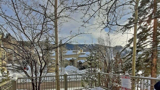 A wooden deck with a hot tub, snow on the ground, and a view of buildings in the background.