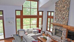 A spacious living room with a stone fireplace, large windows, and a grey sectional sofa.