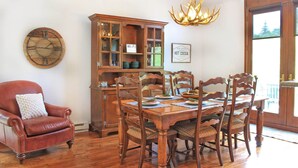 A dining area with a wooden table, chairs, a leather armchair, a wooden cabinet, and a wall clock.