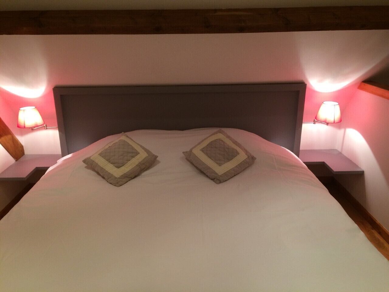 A neatly made bed with two pillows and two bedside lamps on either side.