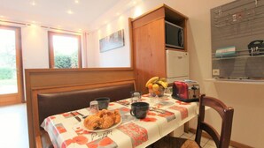 Un coin repas avec une table dressée pour deux personnes, un four à micro-ondes, un grille-pain et un panier de fruits.