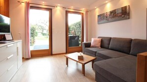 Un salon moderne avec un canapé gris, une table basse en bois et un téléviseur à écran plat posé sur un meuble blanc.