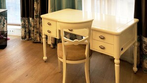 Een kamer met een wit bureau en stoel, een raam met gordijnen, en een uitzicht op gebouwen.