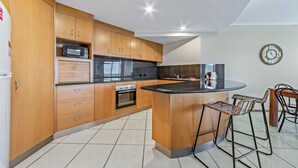 A modern kitchen with wooden cabinets, a built-in oven, a microwave, and a bar area with stools.