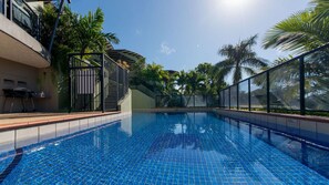 Ein Swimmingpool mit gefliestem Boden, umgeben von einem Zaun und Palmen.