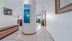 A hallway with a large pillar, a woven bench, and a painting of a tropical landscape.
