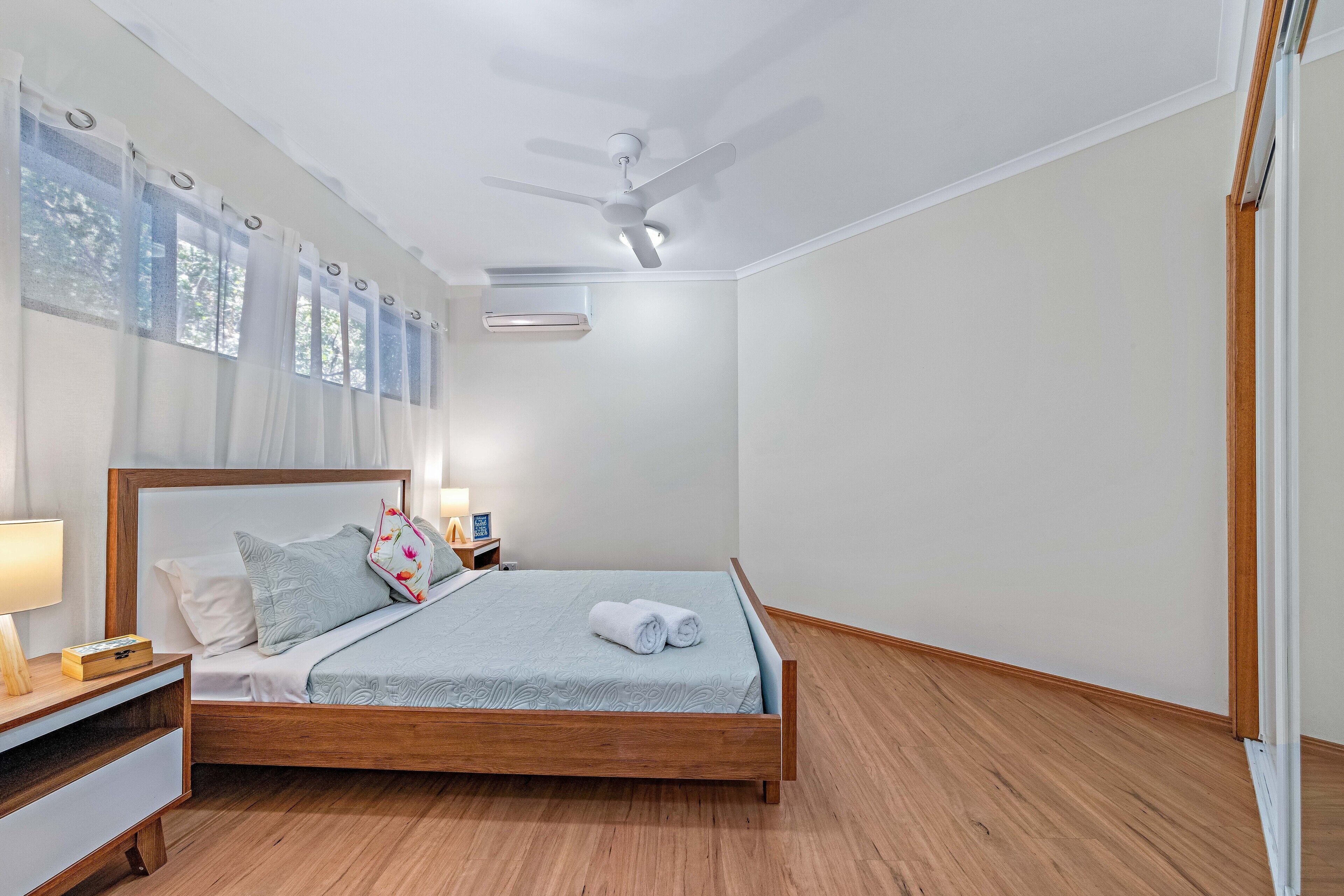A neatly arranged bedroom with a wooden bed, a bedside table with a lamp, and a ceiling fan.
