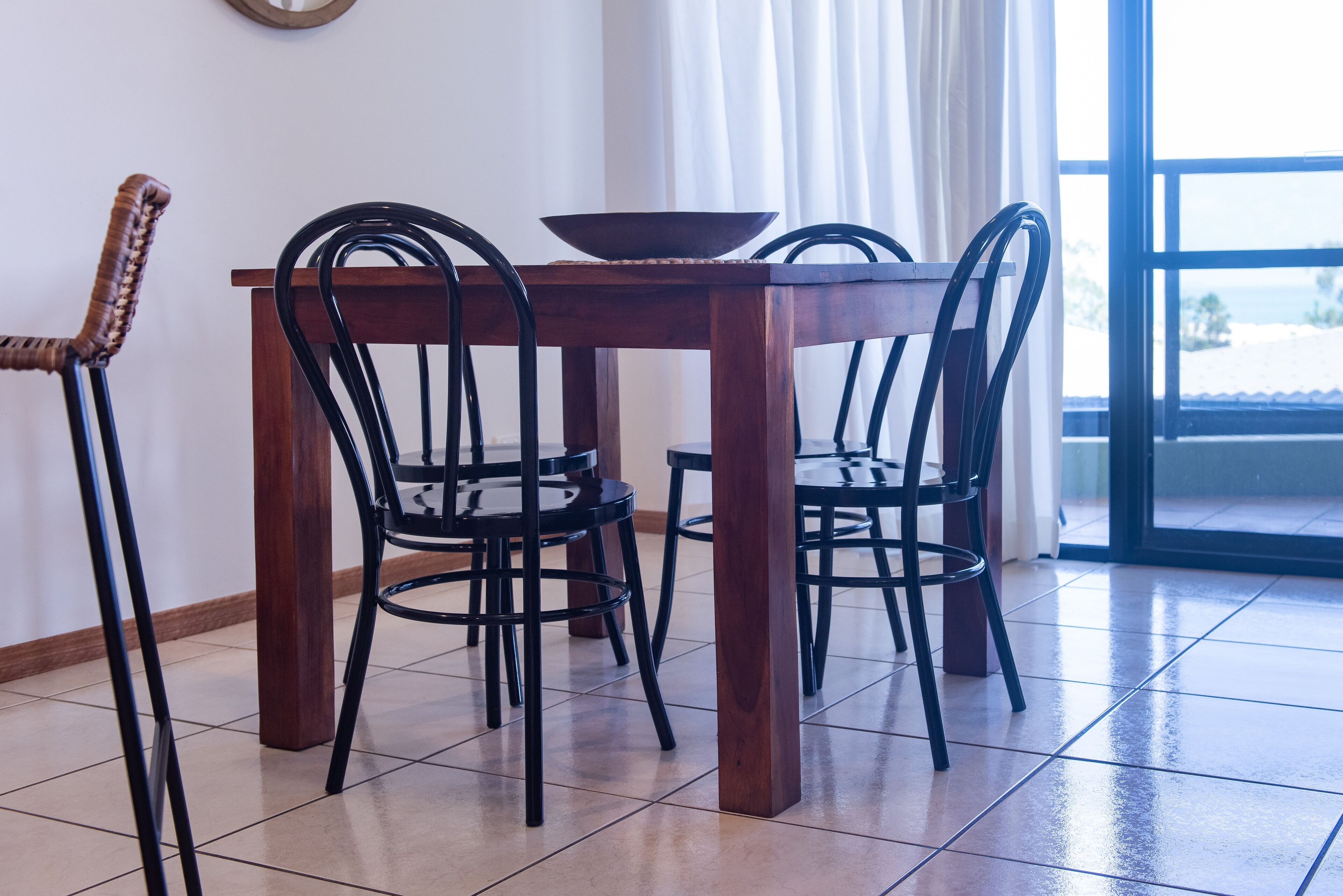 A dining table with four chairs, a bowl, and a window with curtains.