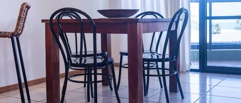 A dining table with four chairs, a bowl, and a window with curtains.
