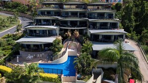 A multi-story hotel with a central swimming pool, outdoor seating, and lush landscaping.