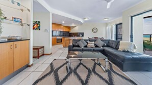A modern living room with a black leather sofa, a glass coffee table, and a patterned rug.