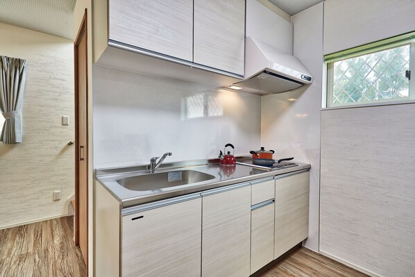 Een moderne keuken met een roestvrijstalen spoelbak, een rode waterkoker en een raam met uitzicht op bomen.