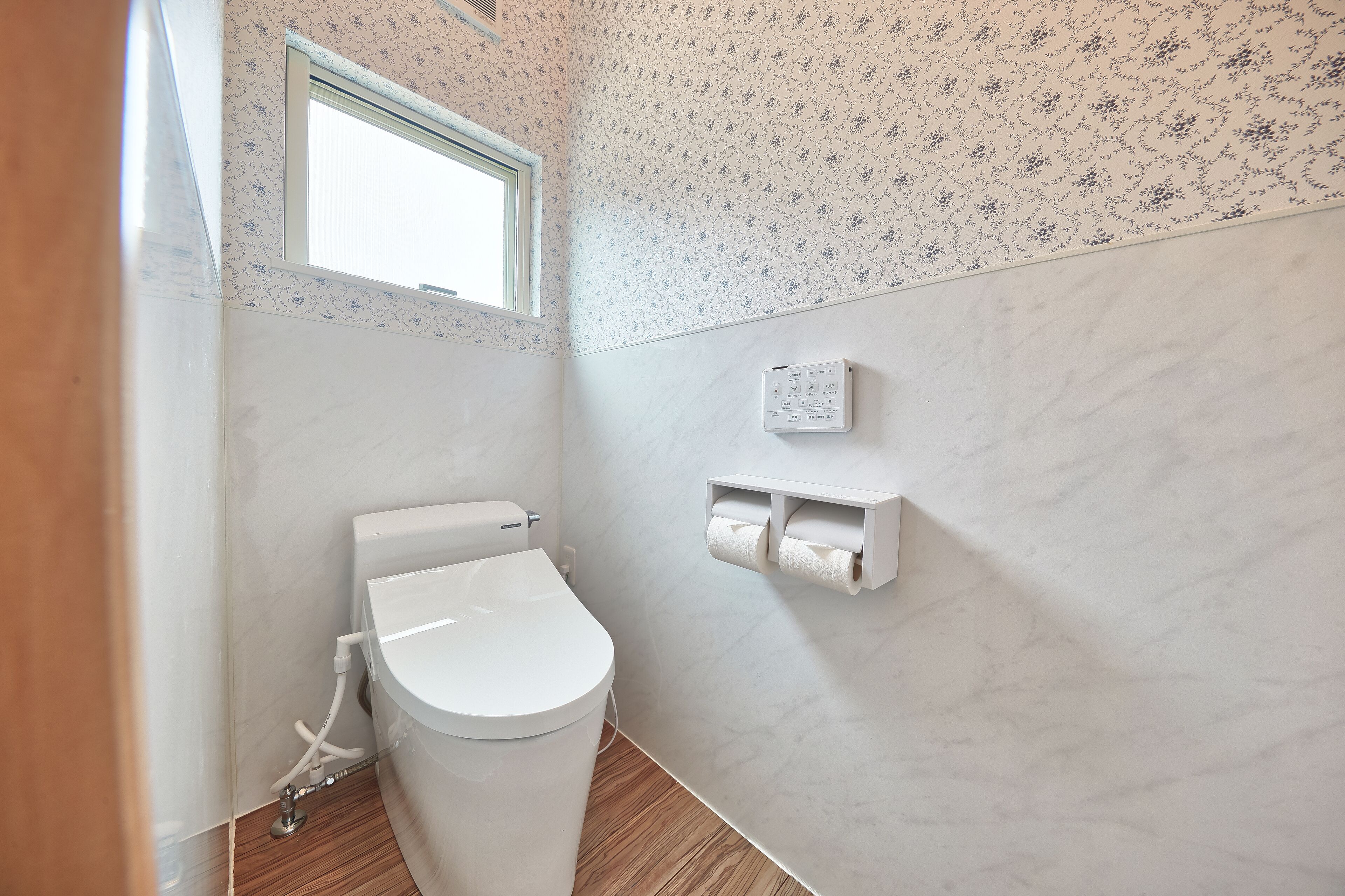 Un baño moderno con inodoro, dispensador de papel higiénico empotrado en la pared y ventana.