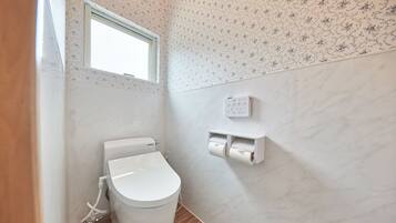 Un baño moderno con inodoro, dispensador de papel higiénico empotrado en la pared y ventana.