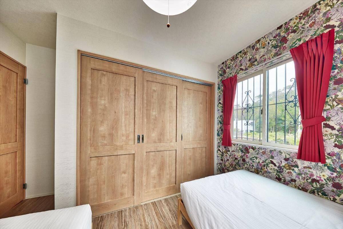 Quarto com guarda-roupa de madeira, uma cama e uma janela com cortinas vermelhas.