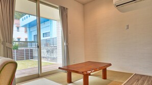A room with a sliding glass door leading to a balcony, a wooden table, tatami mats, and a ceiling air conditioner. - Private Villa Espacio Onna (Onna)