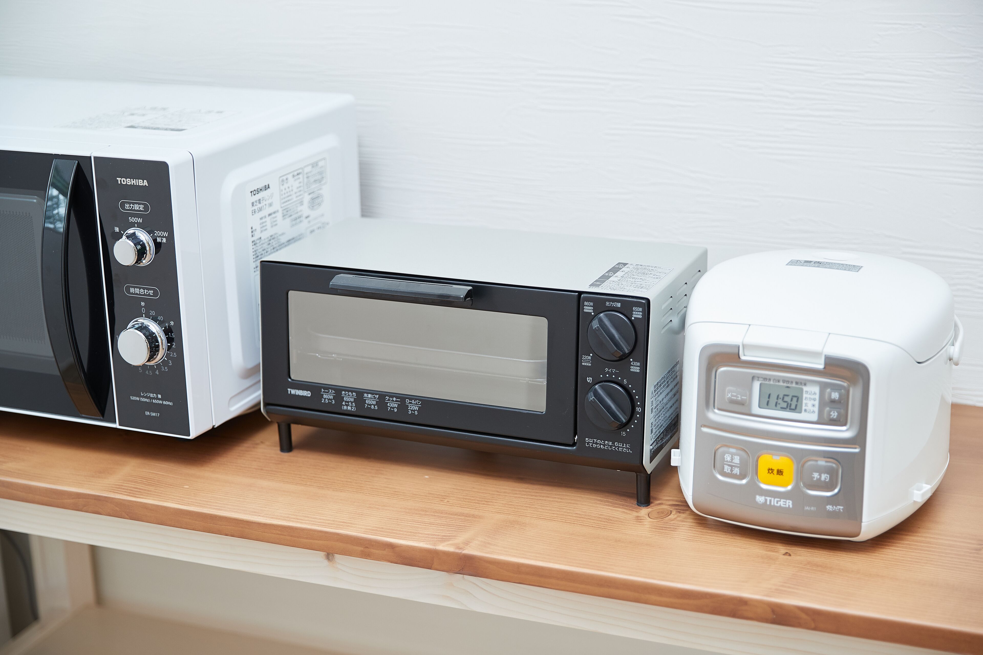 Tres electrodomésticos de cocina: un microondas, un horno tostador y una cocedora de arroz, todos sobre una encimera de madera.