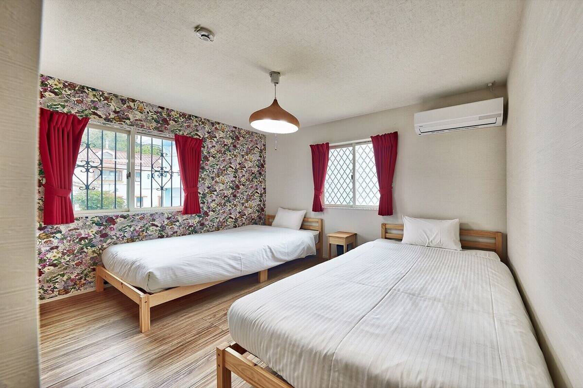 Quarto com duas camas, uma mesa pequena, luminária pendente e aparelho de ar condicionado.