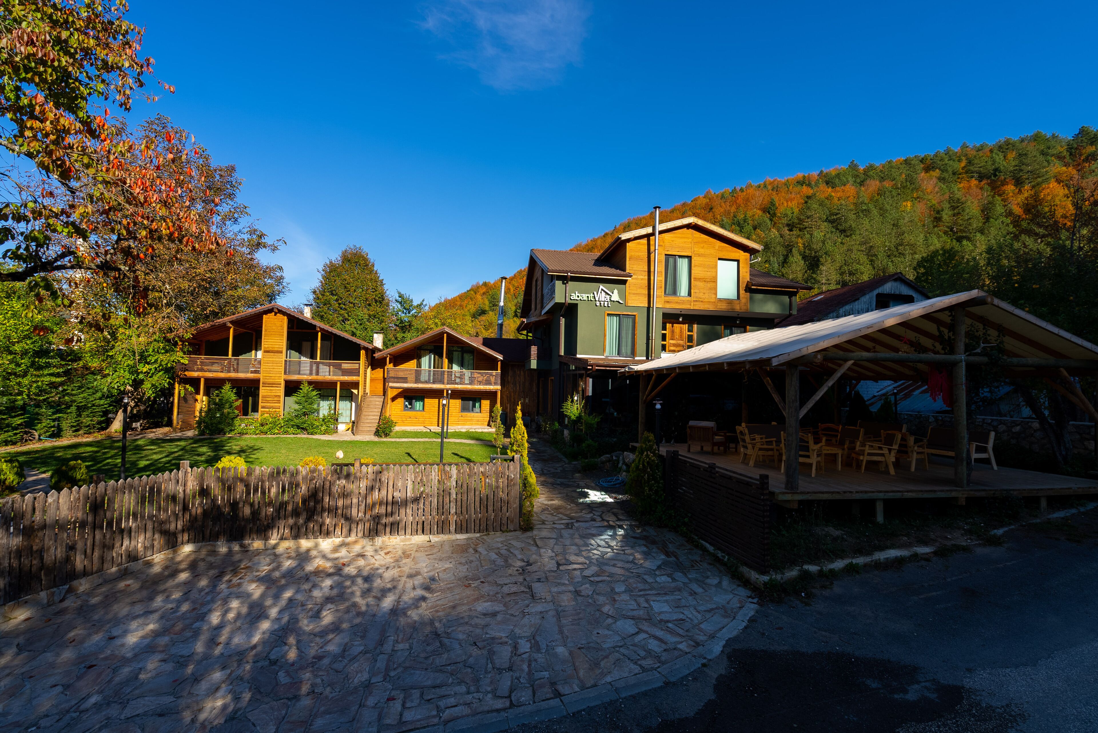 A modern lodge with multiple wooden cabins, a stone-paved courtyard, and a view of a forested hillside.