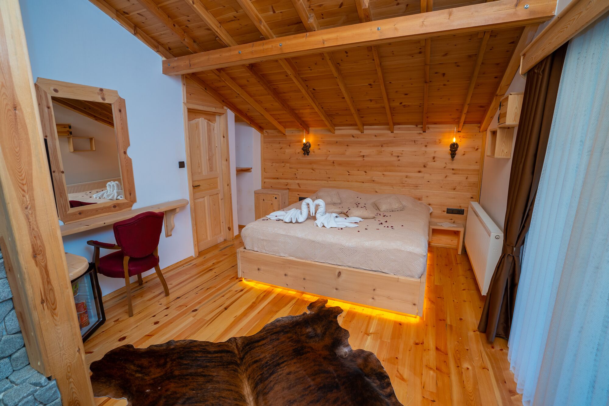 A wooden cabin room with a bed, a chair, a mirror, and a fireplace.