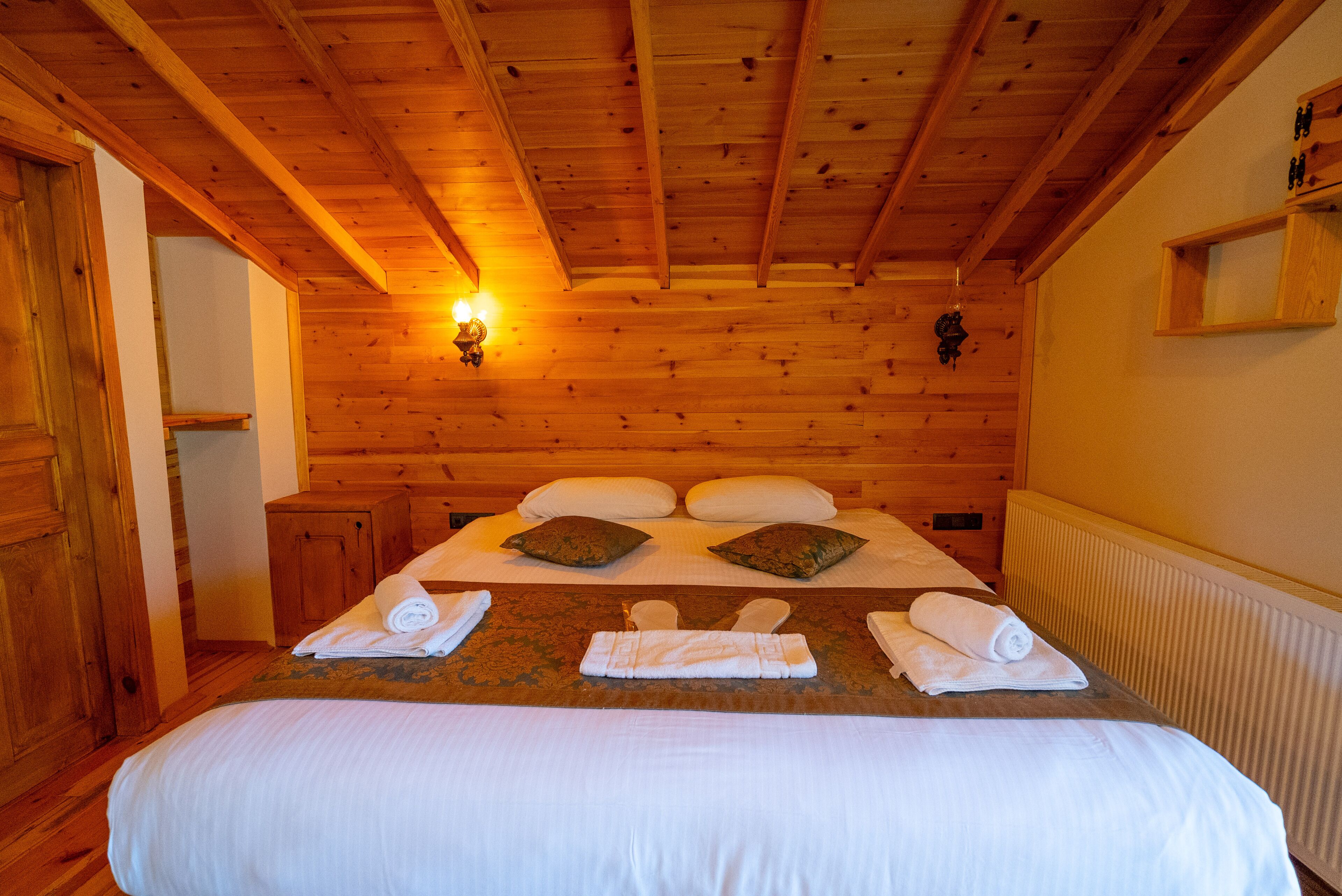 A wooden-paneled room with a bed, towels, and a wall-mounted light fixture.
