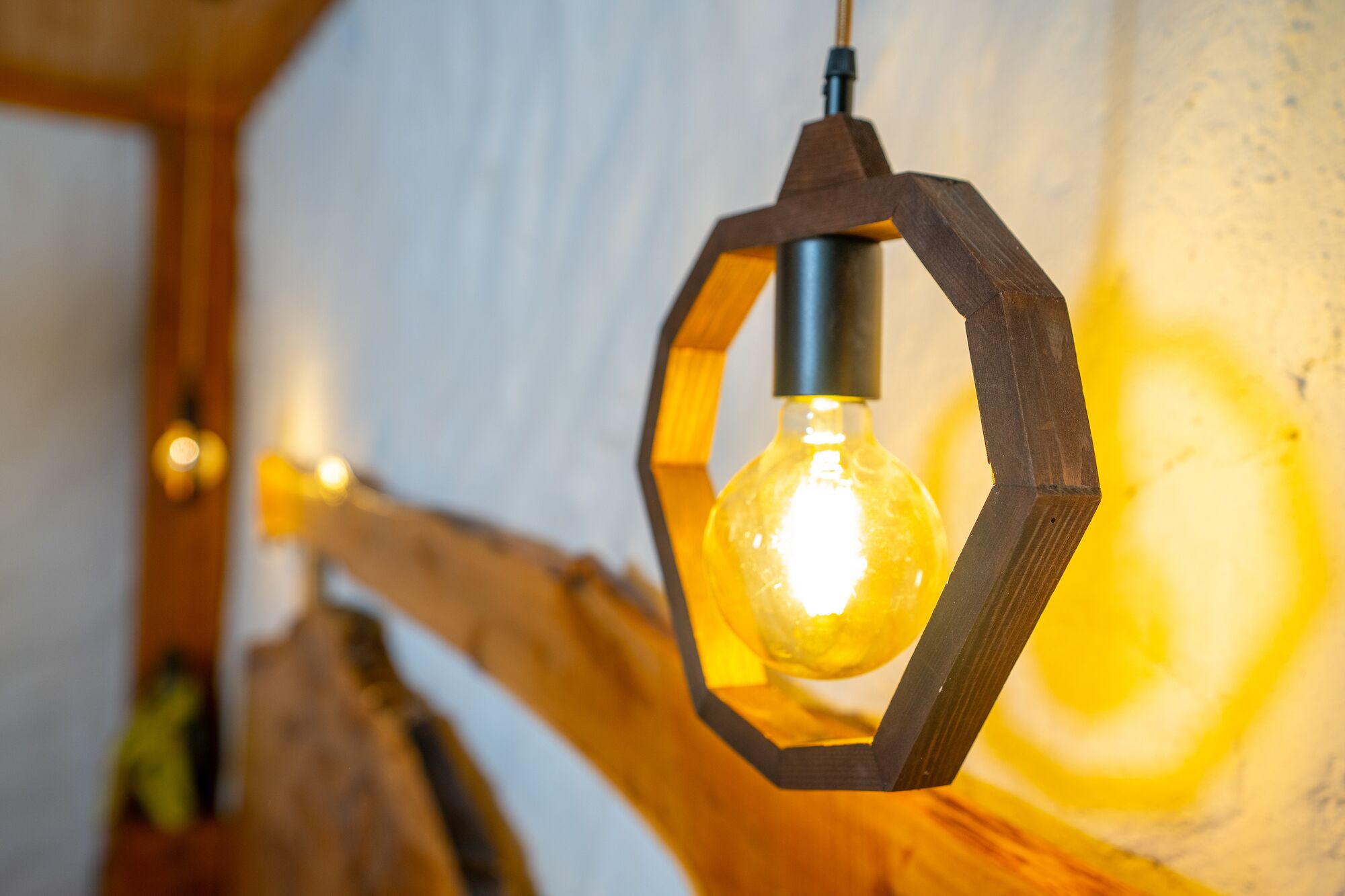 Una lámpara de madera hexagonal con una bombilla encendida.