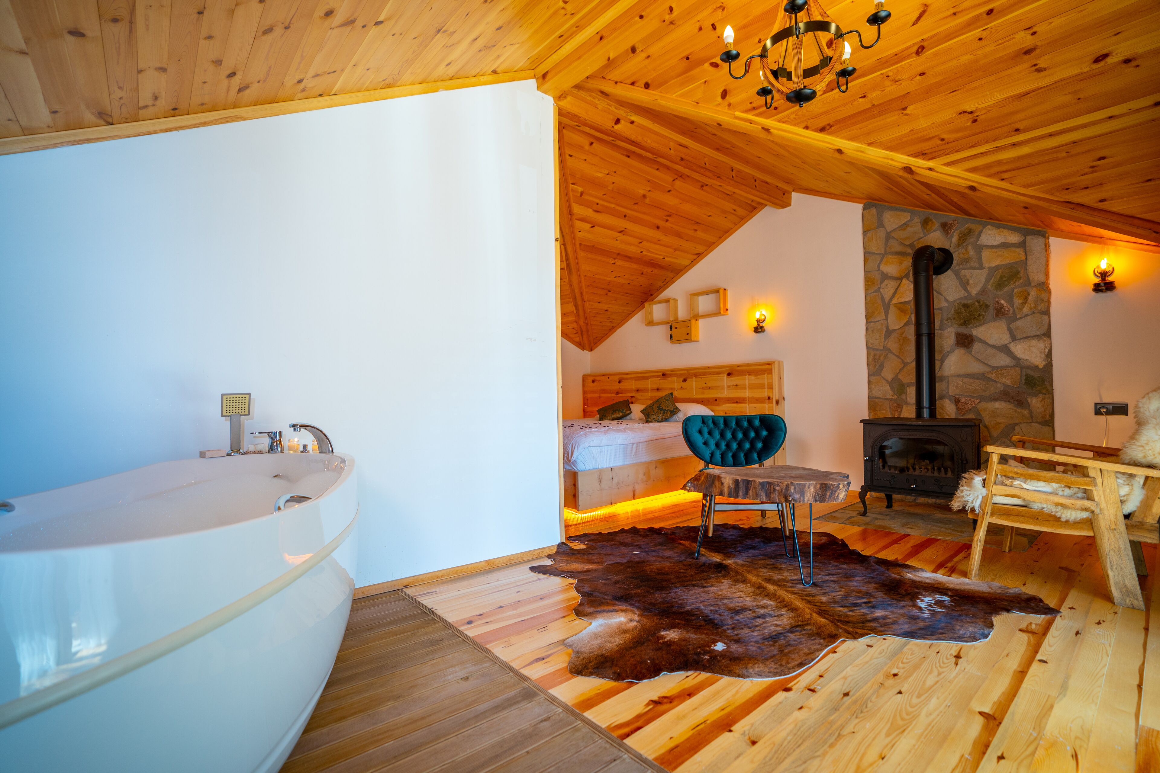 A room with a wooden ceiling, a stone wall, a fireplace, a bed, a bathtub, and a fur rug.